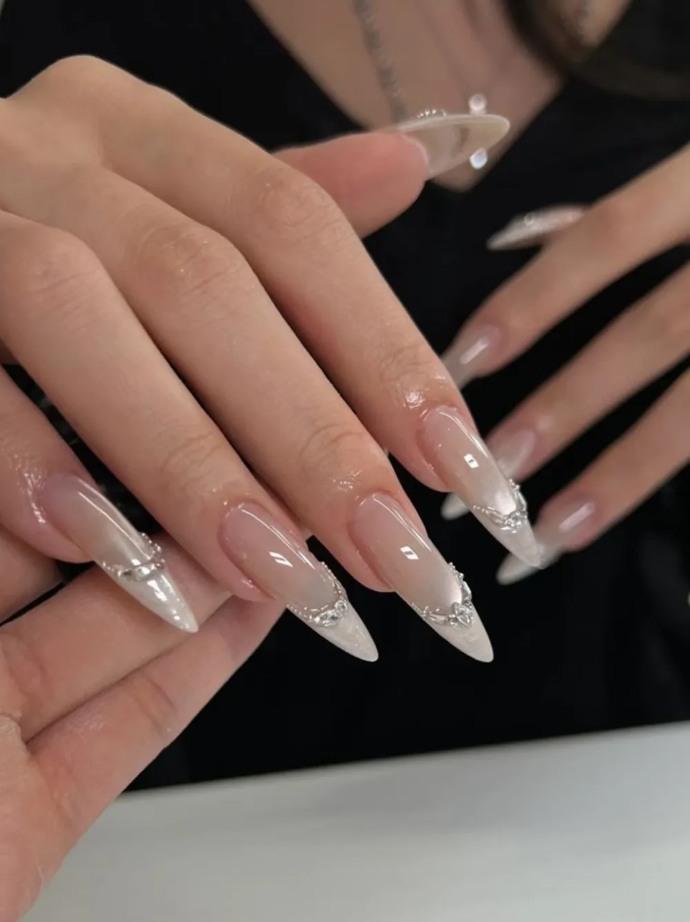 Long almond nails in milky nude ombré with chrome French tips and silver rhinestone accents.