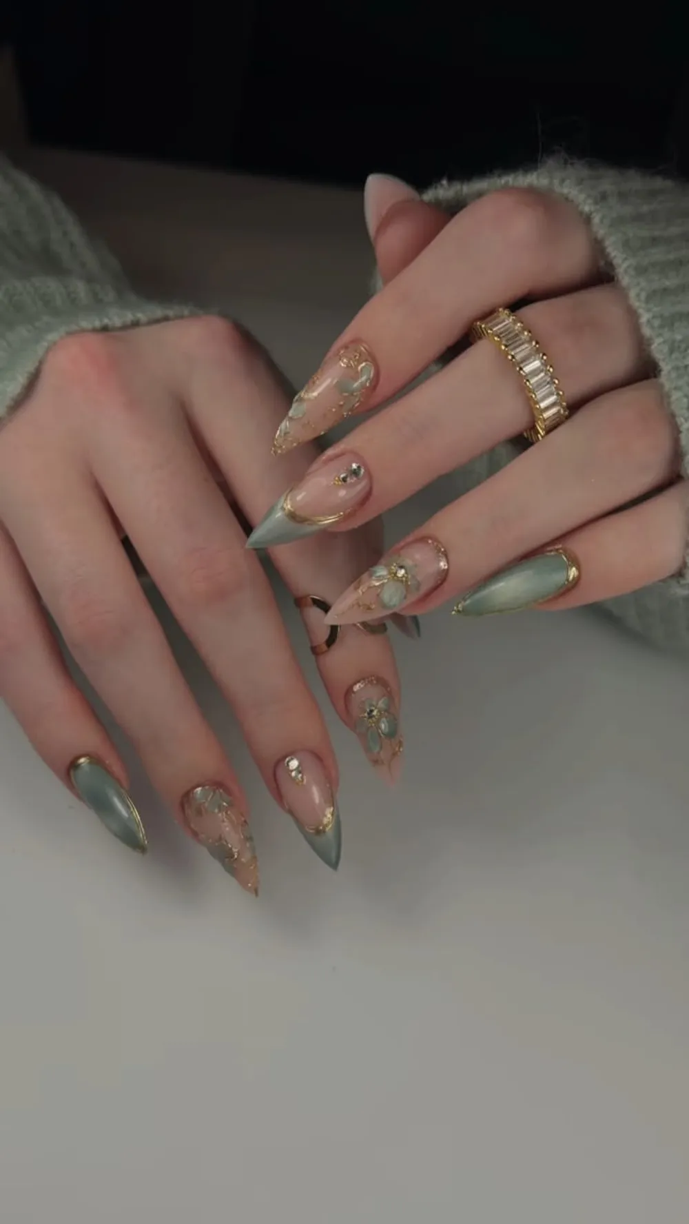Sage-green and nude stiletto nails with gold-leaf foil, gold outlines, and 3D florals.